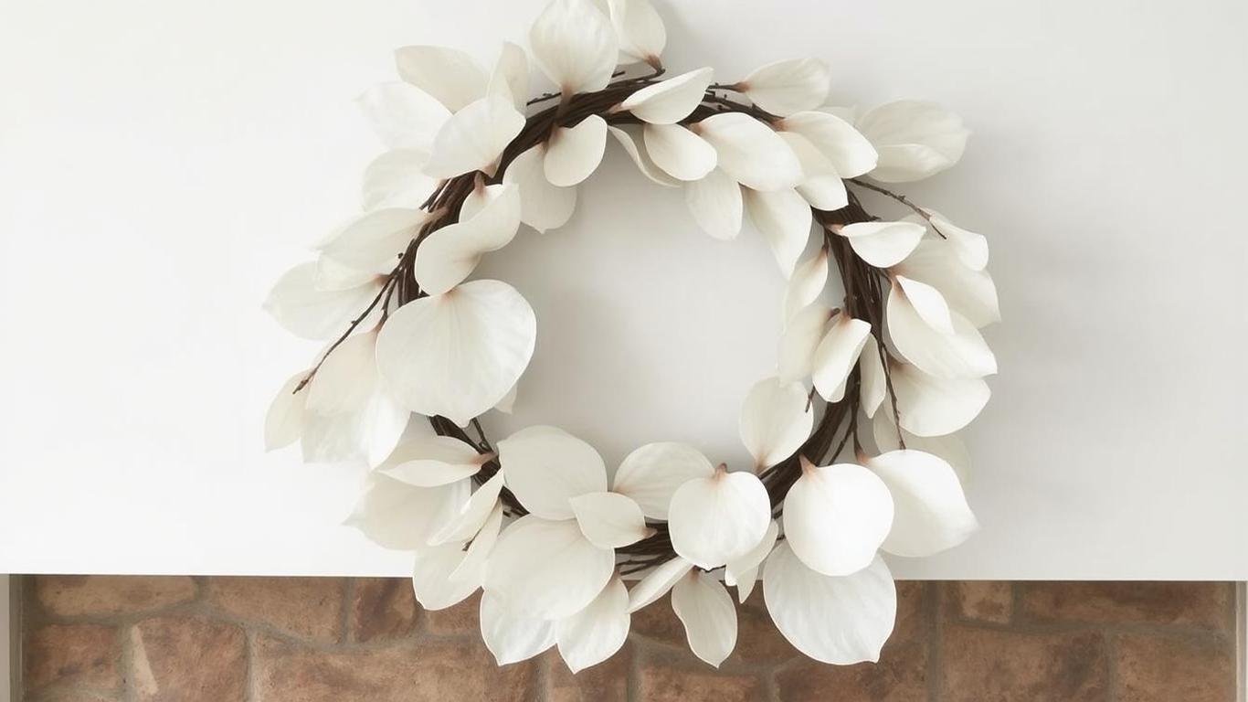 An elegant white magnolia leaf wreath with a polished, clean look. It is displayed indoors above a cozy fireplace, with a neutral background highlighting its simplicity and sophistication.