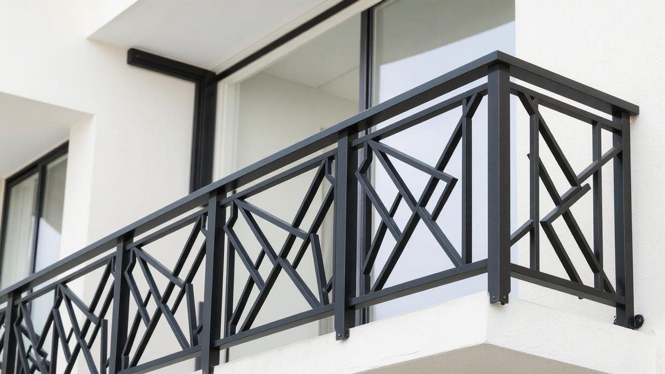 A bold balcony railing with geometric patterns crafted from powder-coated steel in matte black. The design features sharp angles and clean lines, with a minimalist modern apartment backdrop.